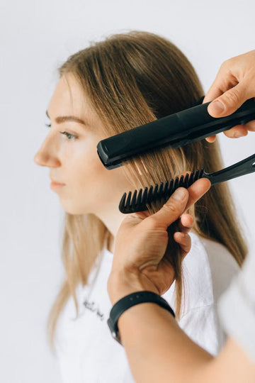 Woman having her hair styled with a flat iron and comb