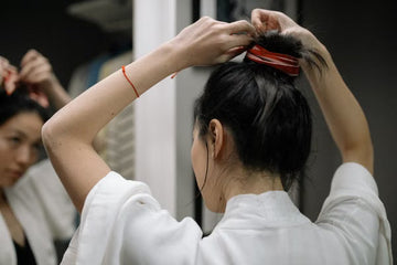 Woman in a bathrobe styling her hair into a bun at a mirror