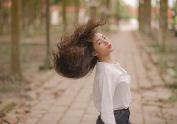 Woman flipping her long, voluminous hair in a park