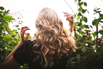 Blonde woman with long waves among sunlit greenery